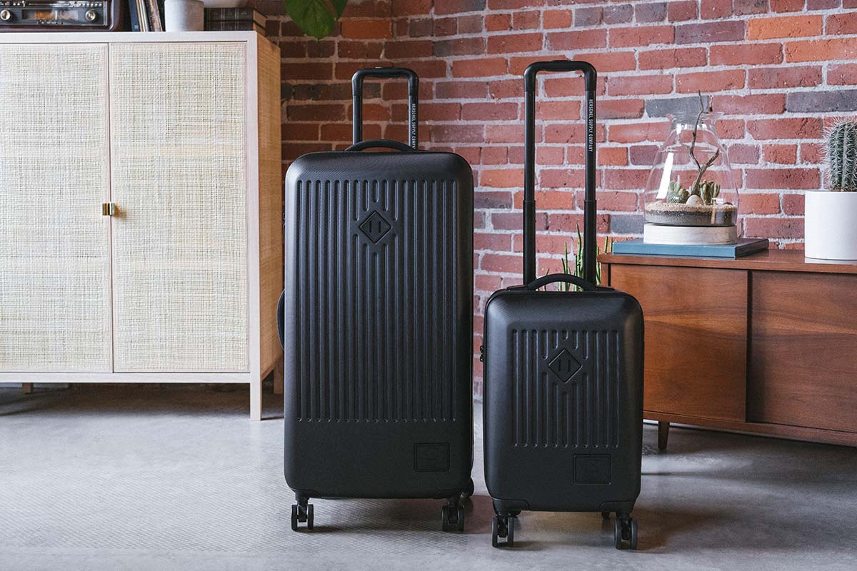 Una Trade Luggage Large y una Trade Luggage Carry-On, la una junto a la otra, en un apartamento con ladrillos a la vista