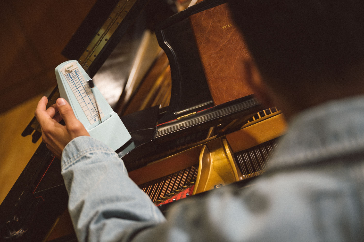 A person at the piano setting their light blue metronome that's sitting on the piano